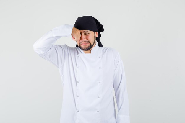 Chef masculin se frottant les yeux en pleurant comme un enfant en uniforme blanc et l'air offensé. vue de face.