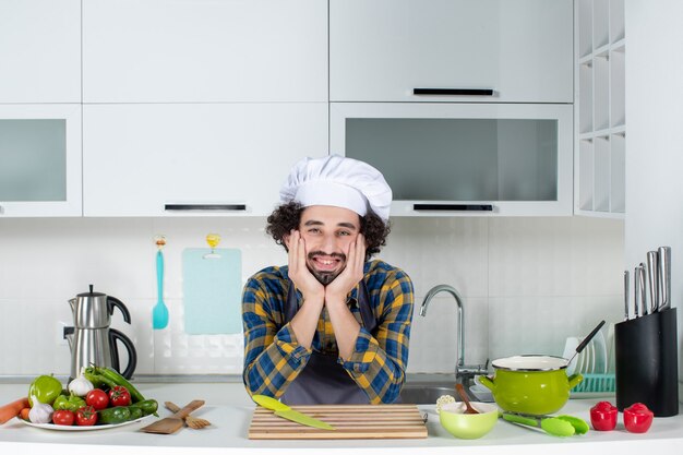 Chef masculin souriant avec des légumes frais posant dans la cuisine blanche