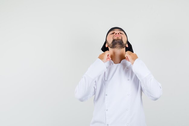 Chef masculin tenant le collier tout en penchant la tête en arrière en uniforme blanc et l'air beau, vue de face.