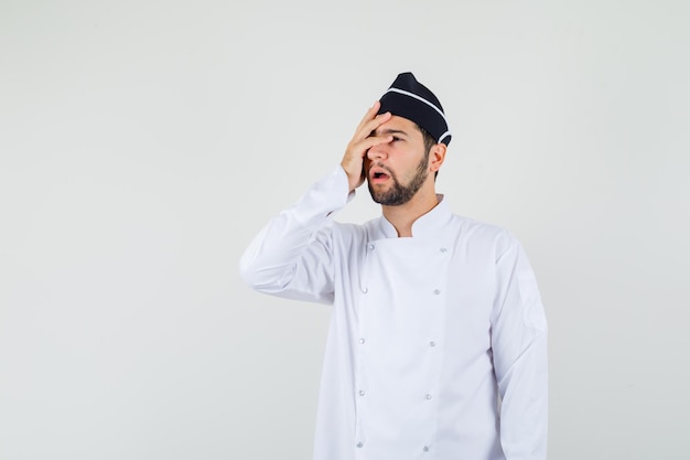 Chef masculin tenant la main sur son visage en uniforme blanc et l'air inquiet, vue de face.