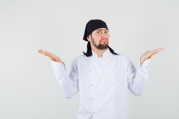 Chef masculin en uniforme blanc montrant un geste impuissant et l'air confus, vue de face.