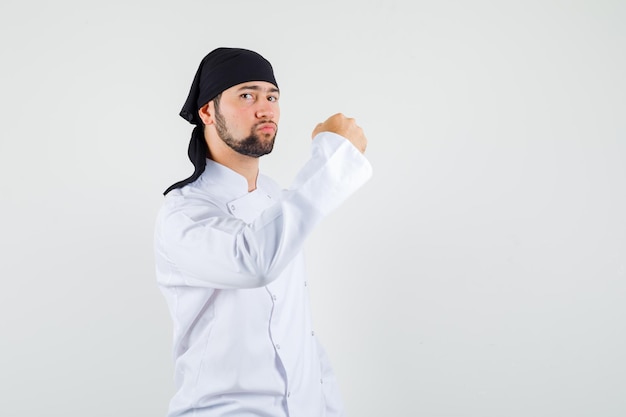 Chef masculin en uniforme blanc montrant le poing fermé et l'air confiant, vue de face.