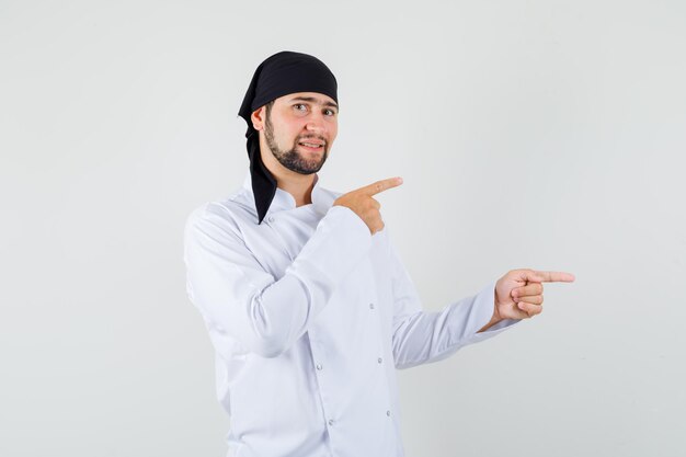 Chef masculin en uniforme blanc pointant les doigts sur le côté et semblant positif, vue de face.