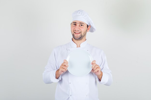 Chef masculin en uniforme blanc tenant une assiette vide et à la bonne humeur