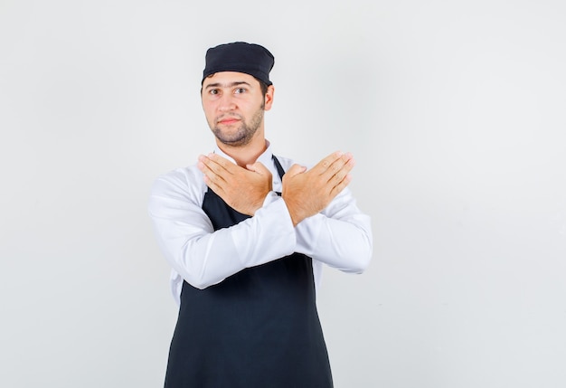 Chef masculin en uniforme, tablier montrant le geste d'arrêt, vue de face.