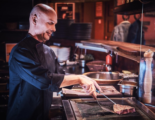 Chef principal concentré portant un uniforme de cuisine délicieux steak de boeuf sur une cuisine dans un restaurant.