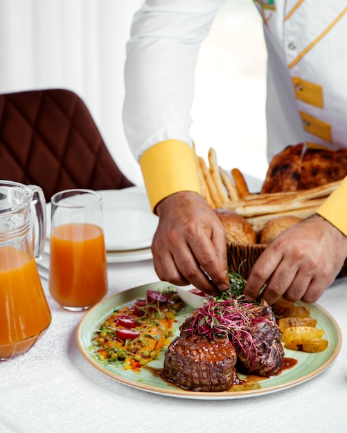 Chef servant des steaks de boeuf grillés avec frites, ketchup et salade