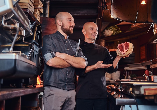 Chef et son assistant présentant un steak frais avant de cuisiner dans une cuisine de restaurant.