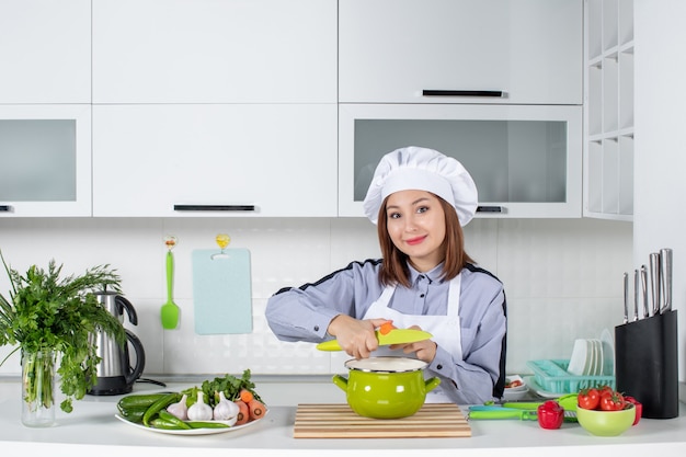 Chef souriant et légumes frais avec équipement de cuisine et couvercle sur la marmite dans la cuisine blanche