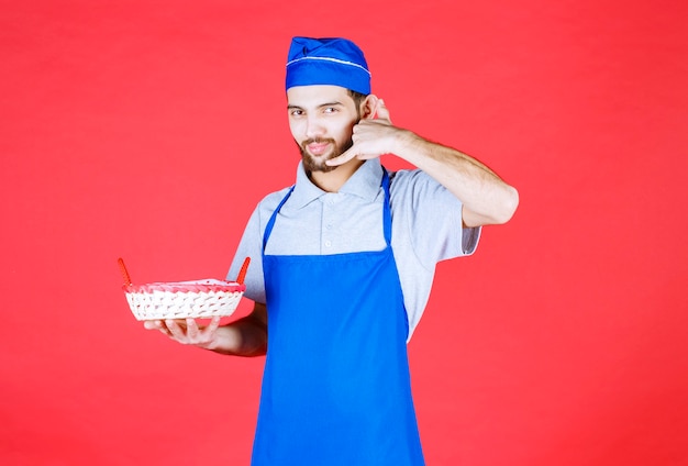 Chef en tablier bleu tenant une corbeille à pain recouverte d'une serviette rouge et demandant un appel.