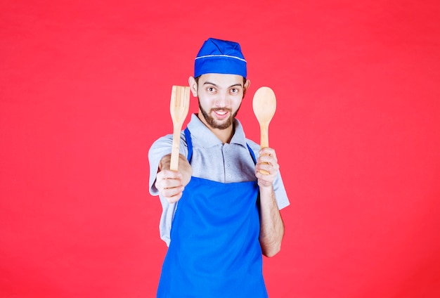 Chef en tablier bleu tenant une cuillère en bois et une spatule.