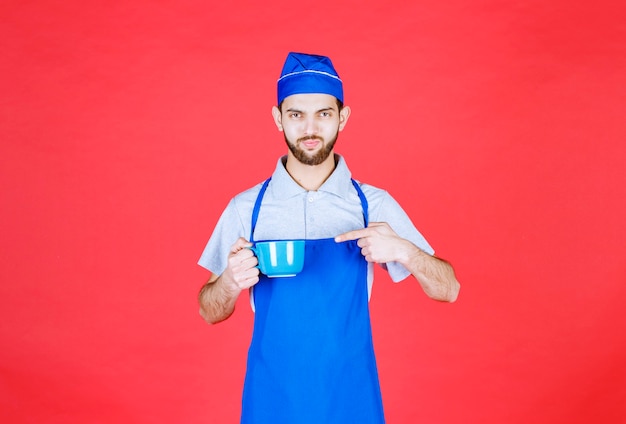 Chef en tablier bleu tenant une tasse en céramique bleue.