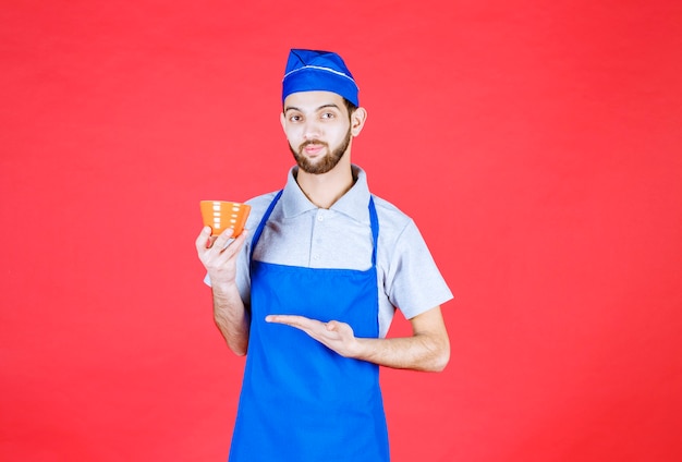 Chef en tablier bleu tenant une tasse en céramique jaune.