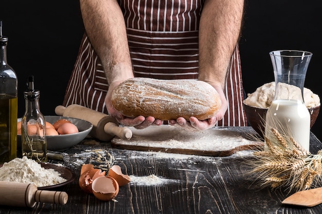 Le chef tient le pain frais à la main. Homme préparant la pâte à table dans la cuisine. Sur fond noir. Concept sain ou de cuisine.