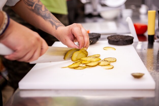 Le chef tranche des cornichons pour un délicieux hamburger au restaurant. La préparation des aliments