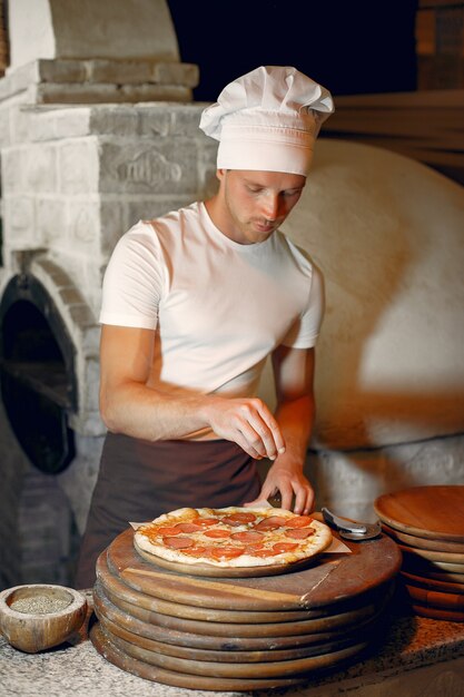 Chef en uniforme blanc prépare une pizza