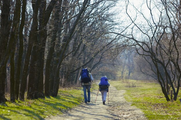 Chemin de deux cœurs aimants. Couple de famille âgés d'homme et femme en tenue de touriste marchant sur la pelouse verte près des arbres en journée ensoleillée. Concept de tourisme, mode de vie sain, détente et convivialité.