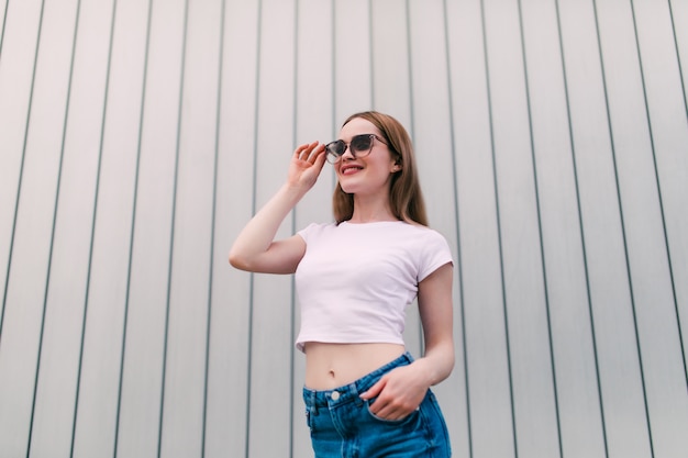 Chemise blanche élégante jeune femme posant sur un mur rayé blanc