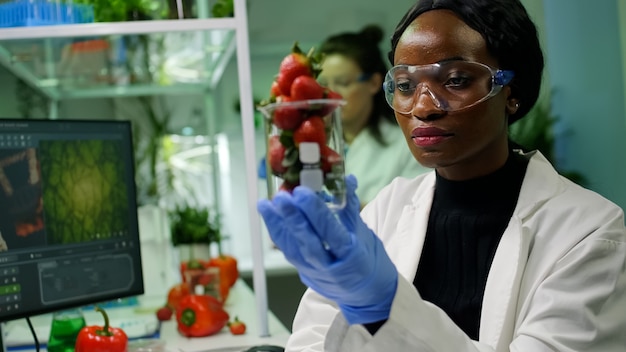 Photo gratuite chercheur africain tenant un verre avec une fraise injectée de pesticides