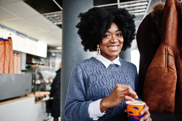 Cheveux bouclés femme afro-américaine porter sur pull posé au café intérieur avec une tasse de thé ou de café