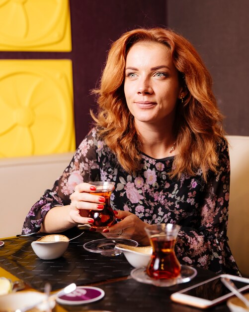 Cheveux roux femme tient un verre armudu avec du thé noir au restaurant