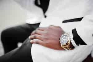 Photo gratuite chic bel homme afro-américain en costume blanc assis sur un banc photo en gros plan de montres dorées à portée de main