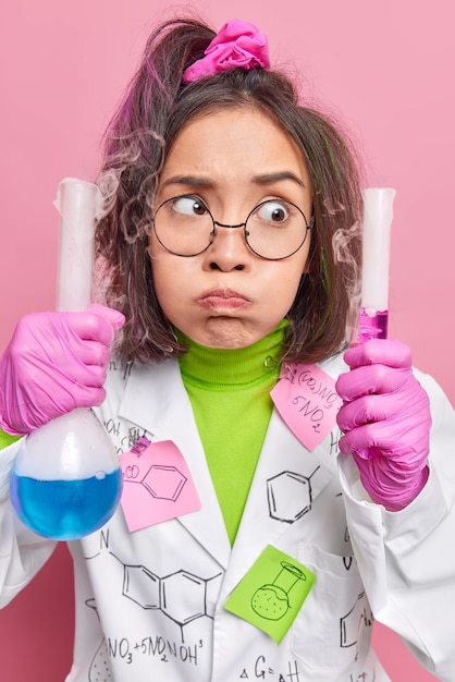 un chimiste en blouse médicale blanche mène une expérience pour la première fois tient un tube à essai et un flacon en verre avec un liquide coloré fonctionne dans un laboratoire scientifique souffle des poses de joues sur le rose