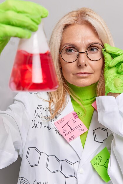 un chimiste fait des recherches scientifiques un test chimique en laboratoire tient un flacon avec un liquide rouge porte des lunettes robe blanche pose à l'intérieur. Biochimie ou développement pharmaceutique