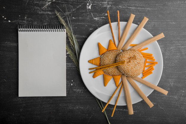 Chips et biscuits dans une assiette blanche sur fond noir avec un livre de cuisine de côté