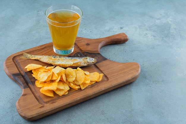 Chips, poisson et verre de bière sur une planche, sur le fond de marbre.