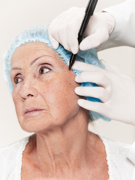 Chirurgien faisant une vérification de la peau d'une femme d'âge moyen avant une chirurgie plastique