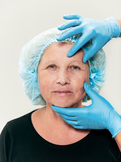 Chirurgien faisant une vérification de la peau d'une femme d'âge moyen avant une chirurgie plastique