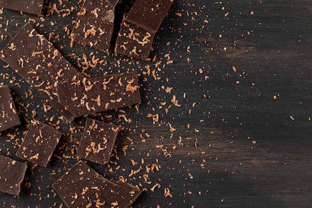 Chocolat râpé avec des barres de choco sur fond sombre, à plat.