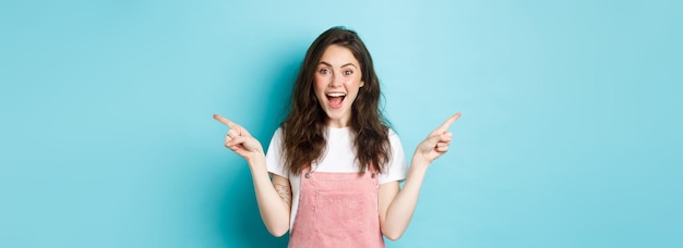 Photo gratuite choisissez votre côté femme excitée souriante criant de joie pointant les doigts sur le côté à gauche et à droite de l'espace de copie montrant une bonne affaire publicitaire debout sur fond bleu