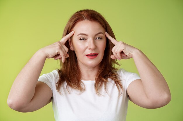 Choix intelligent intrigué réfléchi bienveillant assertif rousse créative femme moyenne toucher les tempes plisser les yeux en réfléchissant à la réflexion sur la pensée utiliser la puissance mentale lire les esprits se tenir debout sur le mur vert