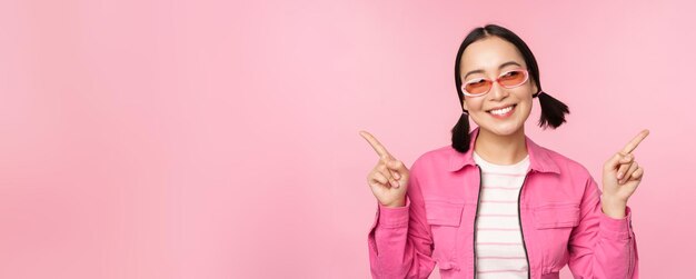 Choix Modèle féminin asiatique fille coréenne élégante pointe les doigts sur le côté montre deux variantes publicité de produit démontrant des articles debout sur fond rose