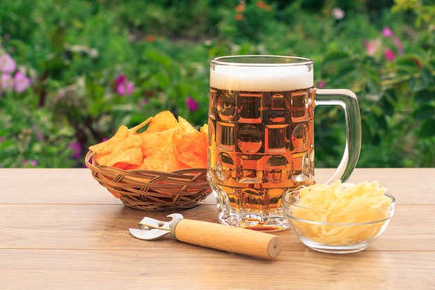 Chope de bière en verre sur table en bois avec croustilles dans un panier en osier, ouvre-porte et calmar séché dans un bol