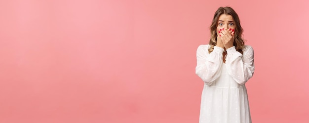 Choqué et anxieux jeune jolie fille concernée en robe blanche haletant fermer la bouche avec les mains regarder w