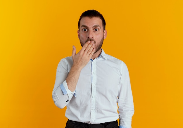 Choqué bel homme met la main sur la bouche isolée sur le mur orange