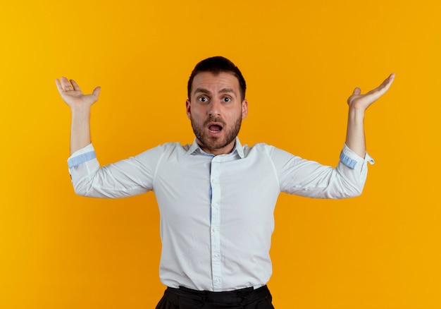 Choqué bel homme se tient avec les mains levées à la recherche d'isolement sur le mur orange