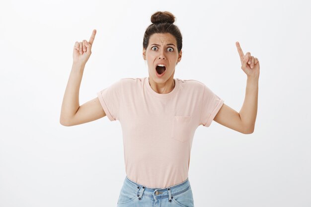 Choqué et confus jeune femme élégante posant contre le mur blanc