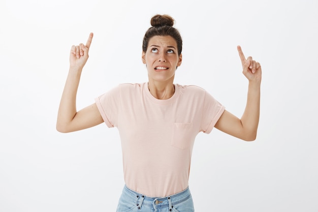 Choqué et confus jeune femme élégante posant contre le mur blanc