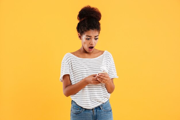 Choqué dame africaine à l'aide et en tapant le téléphone isolé