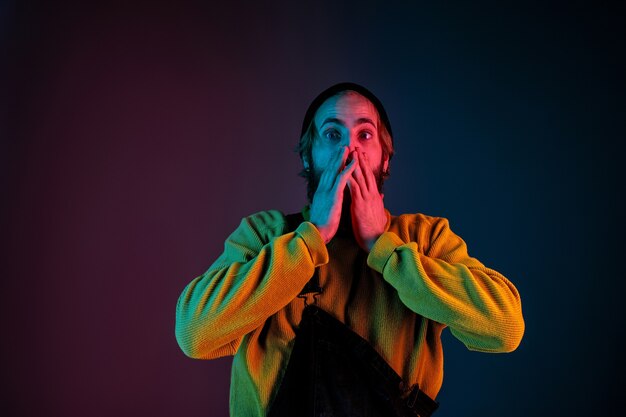 Choqué, étonné. Portrait de l'homme caucasien sur fond de studio dégradé en néon. Beau modèle masculin avec un style hipster. Concept d'émotions humaines, expression faciale, ventes, publicité.