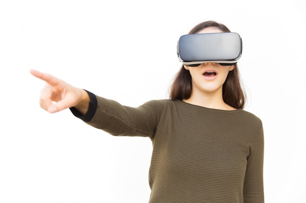 Choqué femme excitée dans le casque VR pointant le doigt loin