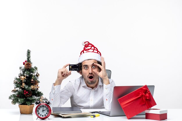 Choqué, homme affaires, à, chapeau père noël, et, tenue, sien, carte bancaire, regarder, quelque chose, soigneusement, dans, bureau, blanc, fond Banque de Photo