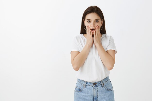 Choqué et intrigué jeune femme posant contre un mur blanc