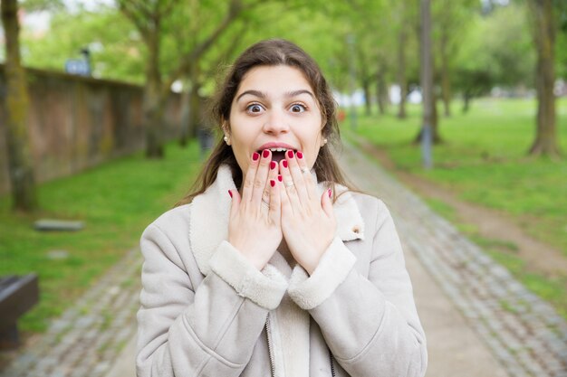 Choqué jeune femme couvrant la bouche avec les mains dans le parc