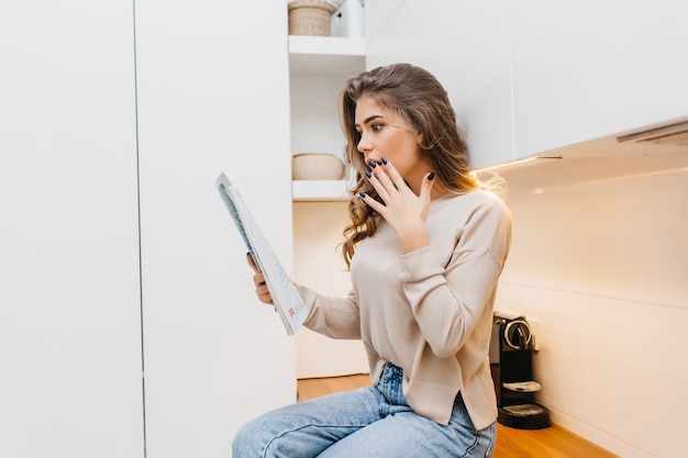 Choqué jeune femme avec des ongles noirs lisant des nouvelles à la maison