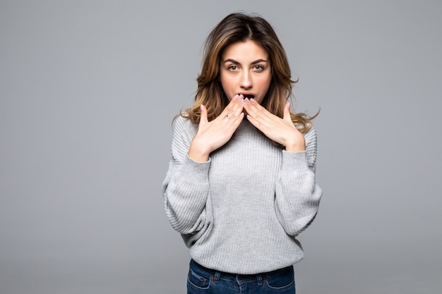 Choqué de jeune femme en pull gris a mis les mains sur les joues isolés sur le mur gris.